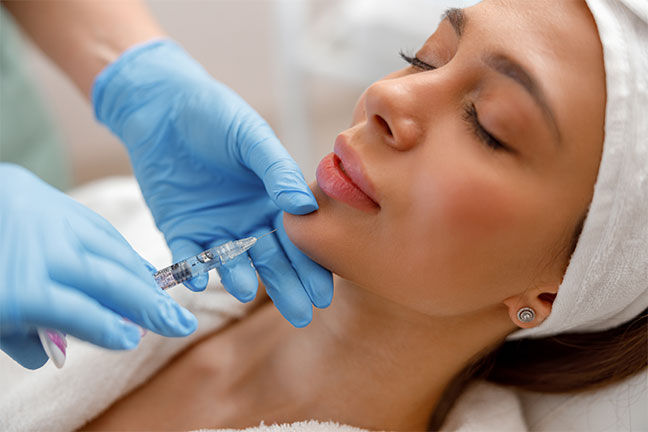 Gloved hand injecting dermal filler into a woman's lip