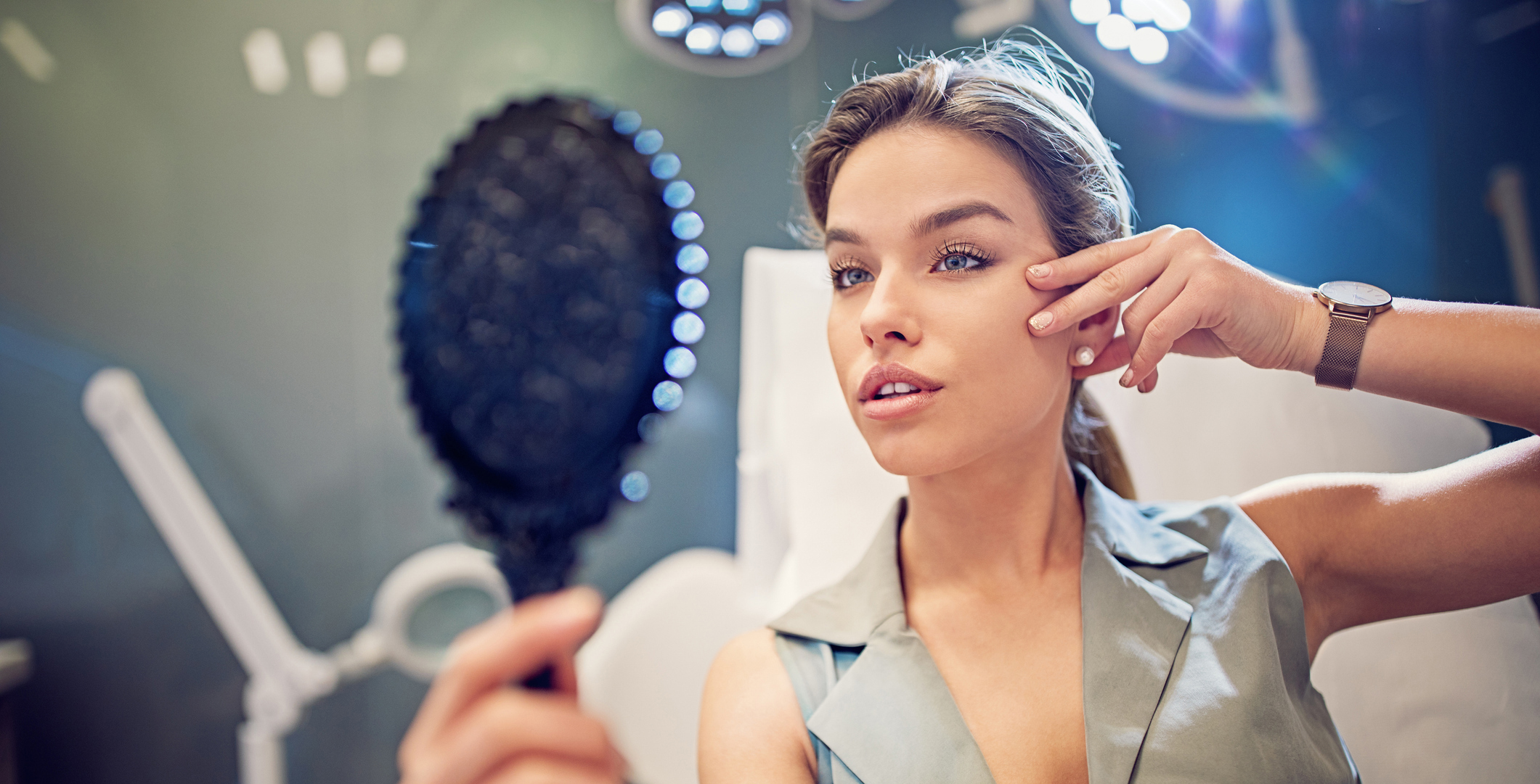 Young woman is looking her face in the mirror after beauty treatment procedure
