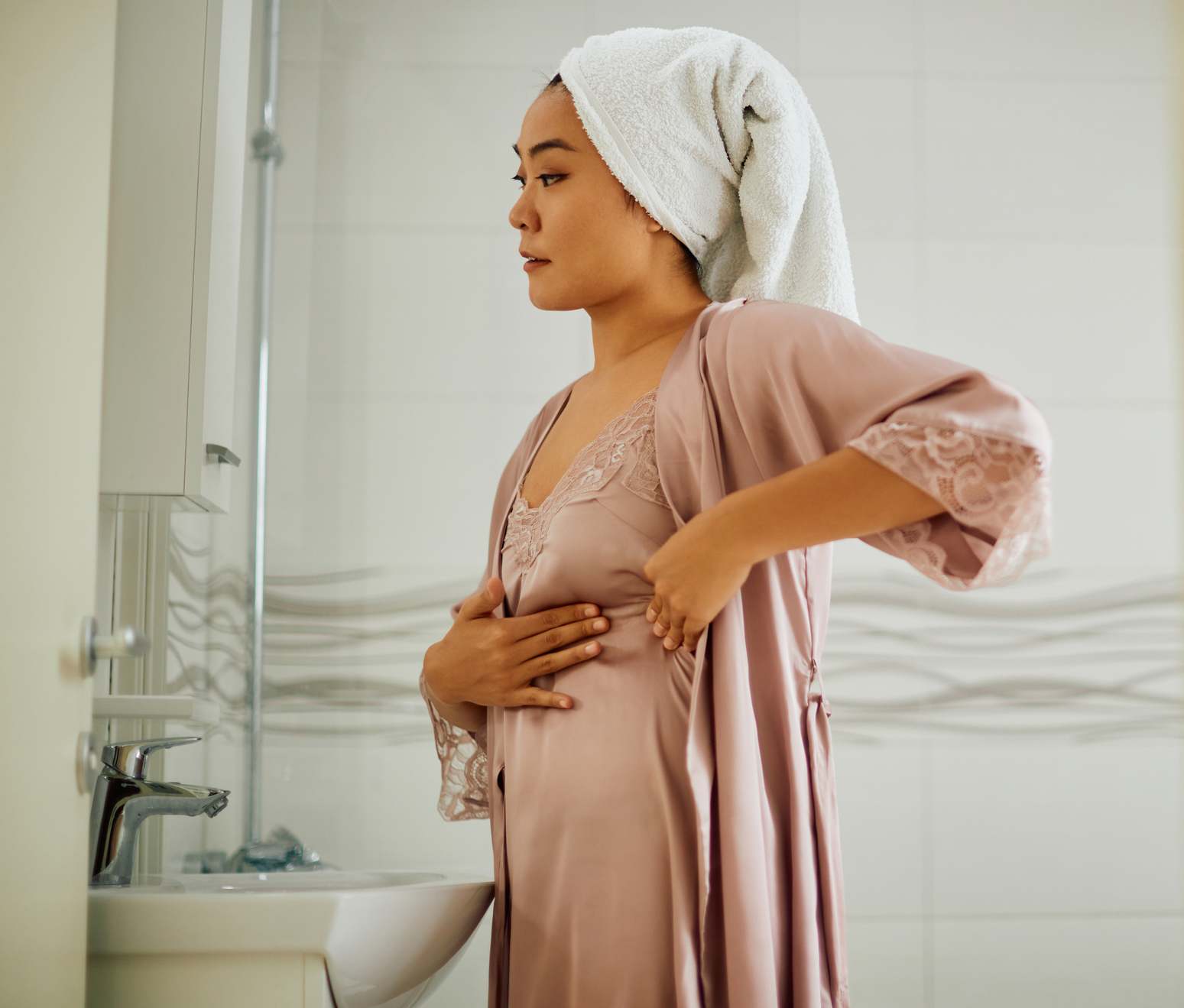 Asian woman doing breast self-exam while looking herself in a mirror in the bathroom. Breast Implant Illness in Bucks County, PA & Hunterdon County, NJ