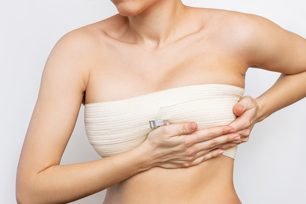 Cropped shot of young woman with elastic bandage after breast augmentation with silicone implants