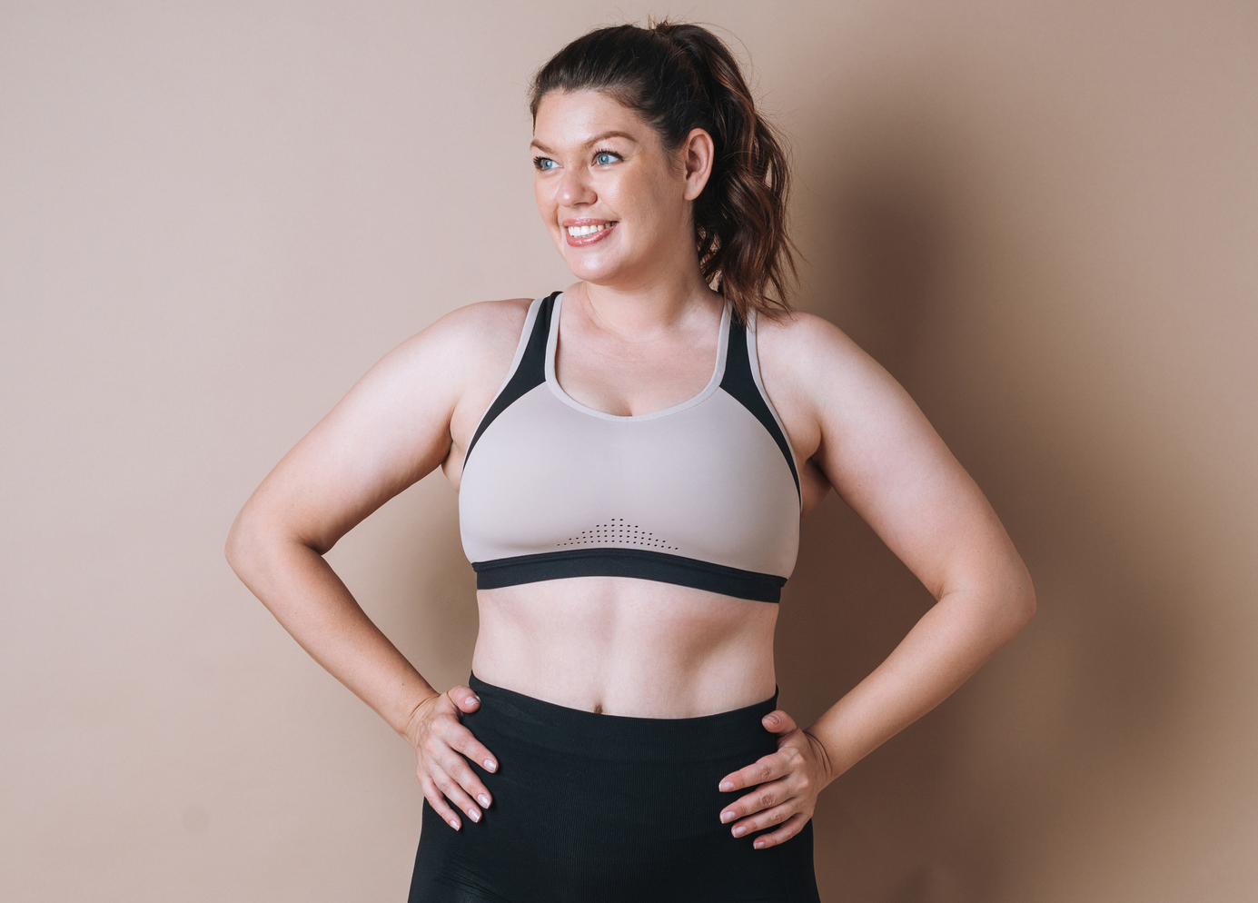 Self loving young woman plus size in sport wear on beige background, body love