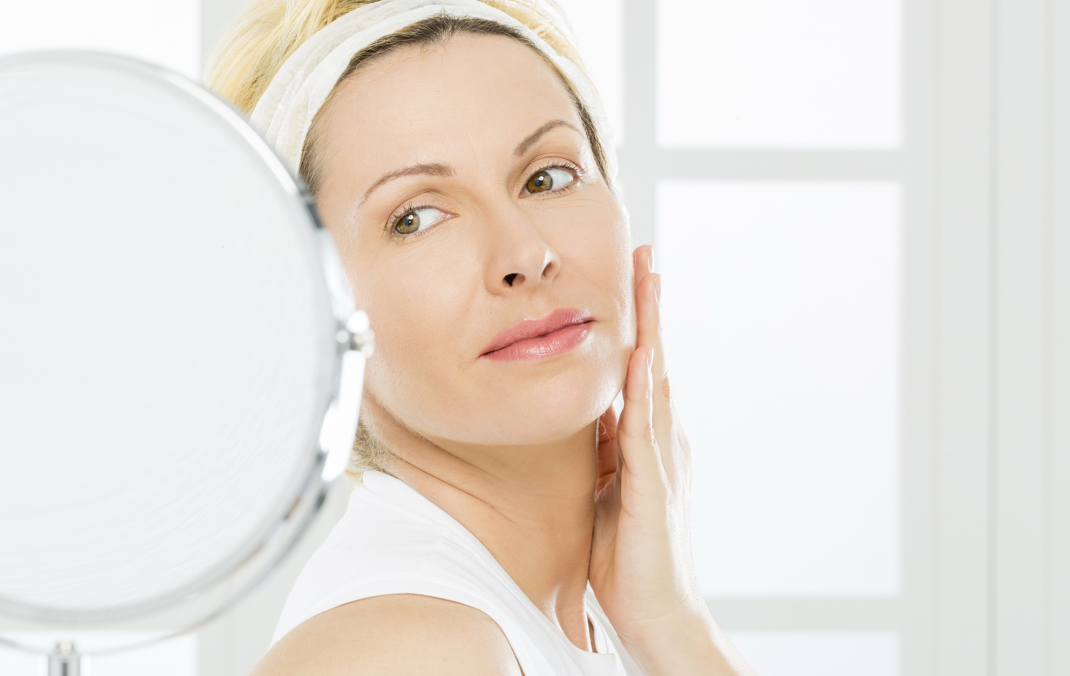 Woman touching her cheek while looking in a mirror