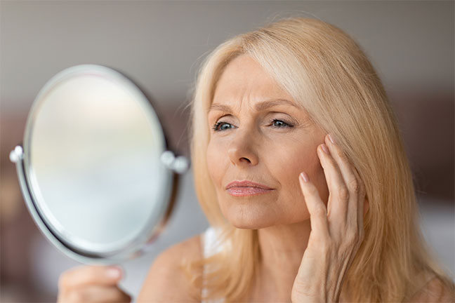 Woman examining forehead wrinkles in a hand mirror